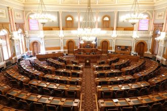 Plenário legislativo vazio, com cadeiras dispostas em semicírculo e grandes lustres no teto.