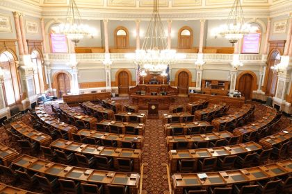 Plenário legislativo vazio, com cadeiras dispostas em semicírculo e grandes lustres no teto.