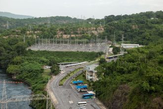 Vista aérea de uma usina elétrica cercada por floresta e próxima a um rio.