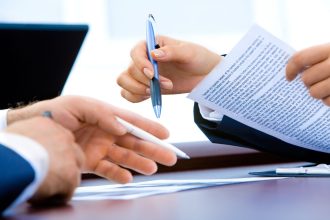 Pessoa analisando documentos e contrato financeiro com uma caneta sobre a mesa