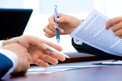 Pessoa analisando documentos e contrato financeiro com uma caneta sobre a mesa