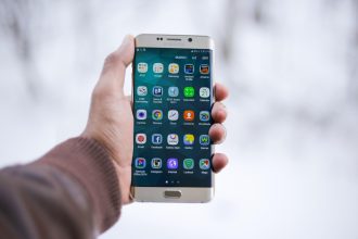 Mãos segurando um smartphone com a tela de aplicativos aberta